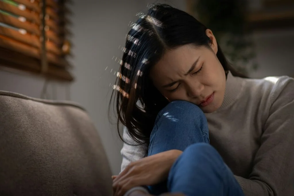 Sad or heart broken Asian woman or Asian girl sitting on a sofa in the living room, anxiety, Lonelin
